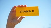 Hand holds piece of paper with Vitamin D against sunny blue sky. Close up.